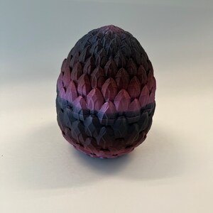 May include: A purple and black dragon egg with a textured, scaly surface. The egg is made of a hard material and has a smooth, rounded shape.