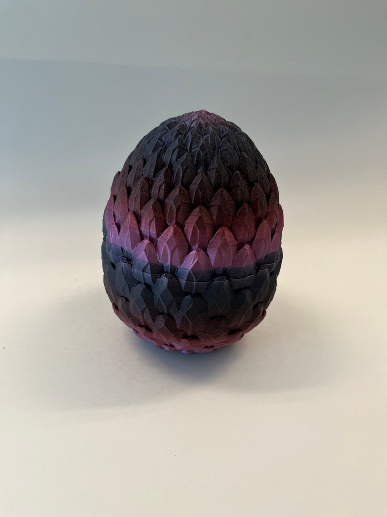 May include: A purple and black dragon egg with a textured, scaly surface. The egg is made of a hard material and has a smooth, rounded shape.