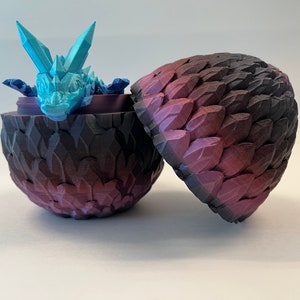 May include: A blue and white dragon figurine inside a purple and black dragon egg. The egg is open and the dragon is looking out.