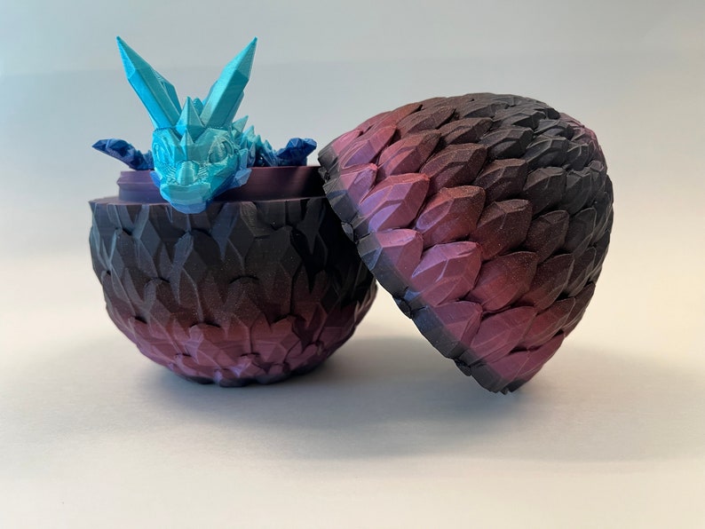 May include: A blue and white dragon figurine inside a purple and black dragon egg. The egg is open and the dragon is looking out.