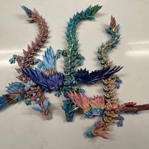 May include: Five origami dragons made of iridescent paper in shades of blue, green, and pink. The dragons are arranged in a circle with their tails intertwined.