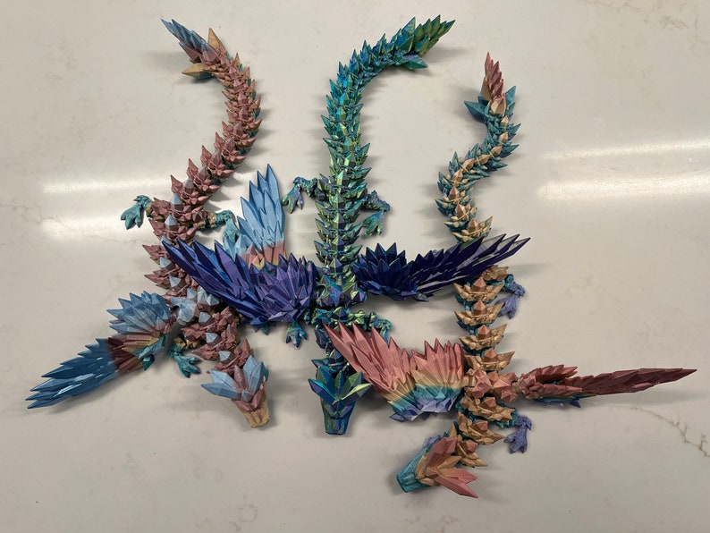 May include: Five origami dragons made of iridescent paper in shades of blue, green, and pink. The dragons are arranged in a circle with their tails intertwined.