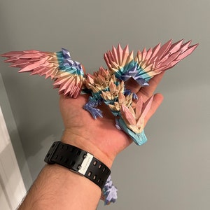May include: A 3D printed dragon figurine with iridescent wings and a crystal-like body. The dragon is painted in shades of pink, blue, and yellow.