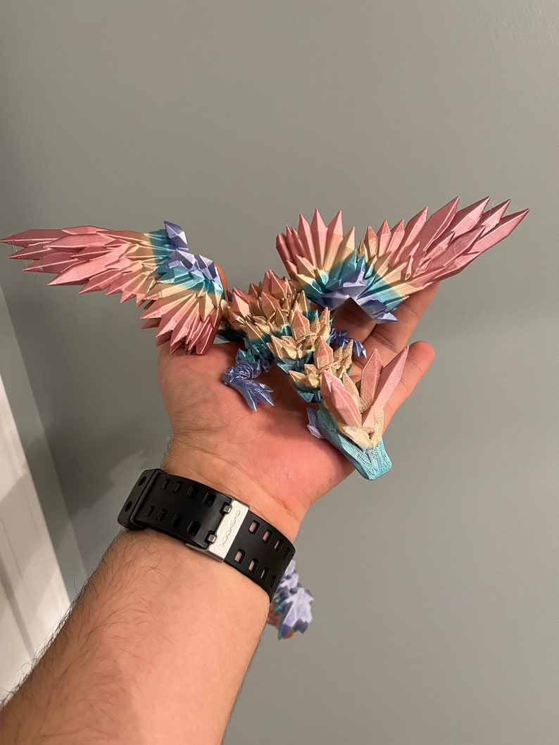 May include: A 3D printed dragon figurine with iridescent wings and a crystal-like body. The dragon is painted in shades of pink, blue, and yellow.