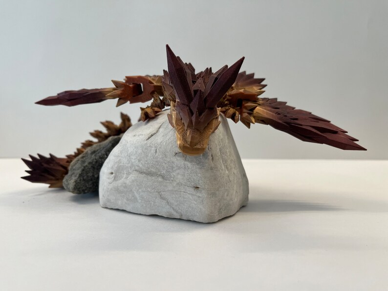 May include: A wooden sculpture of a dragon with brown and red scales, resting on a white rock.