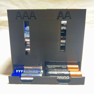 May include: A black plastic battery organizer with two compartments labeled "AAA" and "AA". The organizer is filled with various brand name batteries, including Duracell and Member's Mark.