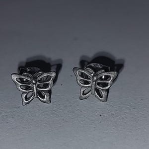 May include: A pair of silver butterfly stud earrings. Each earring features a detailed butterfly design with open wings. The earrings are small and delicate, perfect for everyday wear. The metal has a slightly aged appearance.