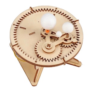 May include: A wooden model of a solar system with gears and planets. The planets are white styrofoam balls and the sun is a small orange ball. The model is on a wooden base.