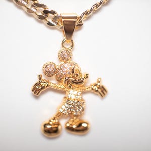 May include: A gold-tone pendant necklace featuring a Mickey Mouse charm with clear cubic zirconia stones. The chain is a thick, gold-tone curb chain.