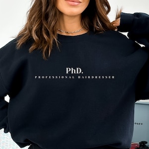Pode incluir: Camisola de moletom preta com o texto "PhD. PROFESSIONAL HAIRDRESSER" impresso em branco na frente.