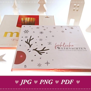 Könnte beinhalten: Zwei Schachteln Schokolade mit Weihnachtsmotiv. Die Schachtel links ist weiß mit einem goldenen 'M' und dem Text 'Fin' und 'GROSSE VIELFA'. Die Schachtel rechts ist weiß mit einem roten Ornament, Rentiergeweih, Schneeflocken und dem Text 'fröhliche WEIHNACHTEN UND EIN GLÜCKLICHES NEUES JAHR' und 'merci'.