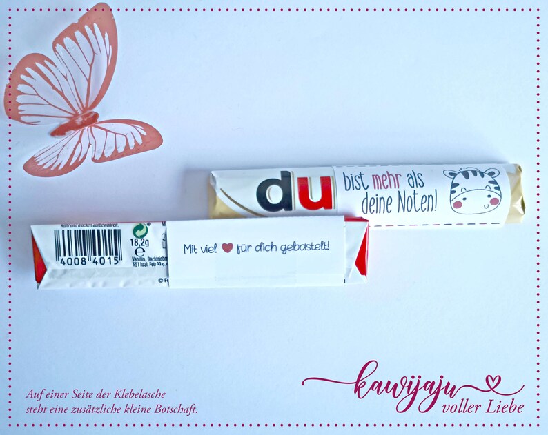 Puede incluir: Una tarjeta blanca con una mariposa coral y dos barras de chocolate. Una barra tiene la palabra "du" en rojo. La otra barra tiene una ilustraci&oacute;n de cebra y el texto "bist mehr als deine Noten!". La tarjeta tambi&eacute;n tiene texto en alem&aacute;n.