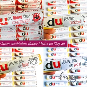 Puede incluir: Una colecci&oacute;n de barras de chocolate con etiquetas personalizadas. Las etiquetas presentan la palabra "du" en rojo y blanco, junto con varias frases alemanas e ilustraciones de dibujos animados. Las barras est&aacute;n dispuestas en una cuadr&iacute;cula, mostrando diferentes dise&ntilde;os.
