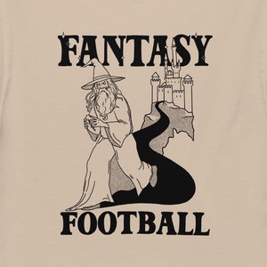 May include: A tan t-shirt with a black graphic of a wizard walking towards a castle with the text "Fantasy Football".
