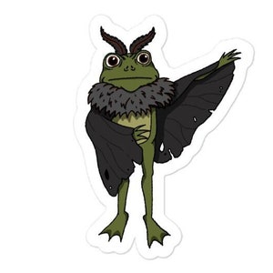 Op de afbeelding: Een groene kikker die een zwart mottenkostuum draagt met bruine antennes en een bontkraag. De kikker staat met zijn rechterarm omhoog en zijn linkerarm langs zijn zijde.