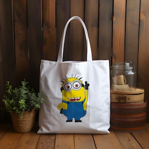 May include: White canvas tote bag with a yellow minion character wearing blue overalls and a black eye patch. The minion is smiling and holding up one finger.