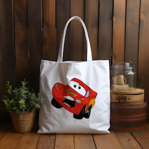 May include: White canvas tote bag with a red cartoon car printed on the front. The car has a smiling face and the words "Lightning McQueen" printed on the side.