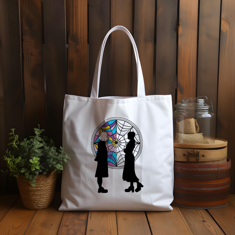May include: White tote bag with a colorful spiderweb design and two black silhouettes of people standing in front of it.