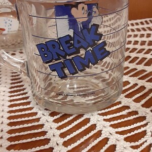 Puede incluir: Una taza de vidrio transparente con un dise&ntilde;o azul y blanco con Mickey Mouse y el texto "Break Time". La taza tiene un asa y est&aacute; decorada con l&iacute;neas azules.