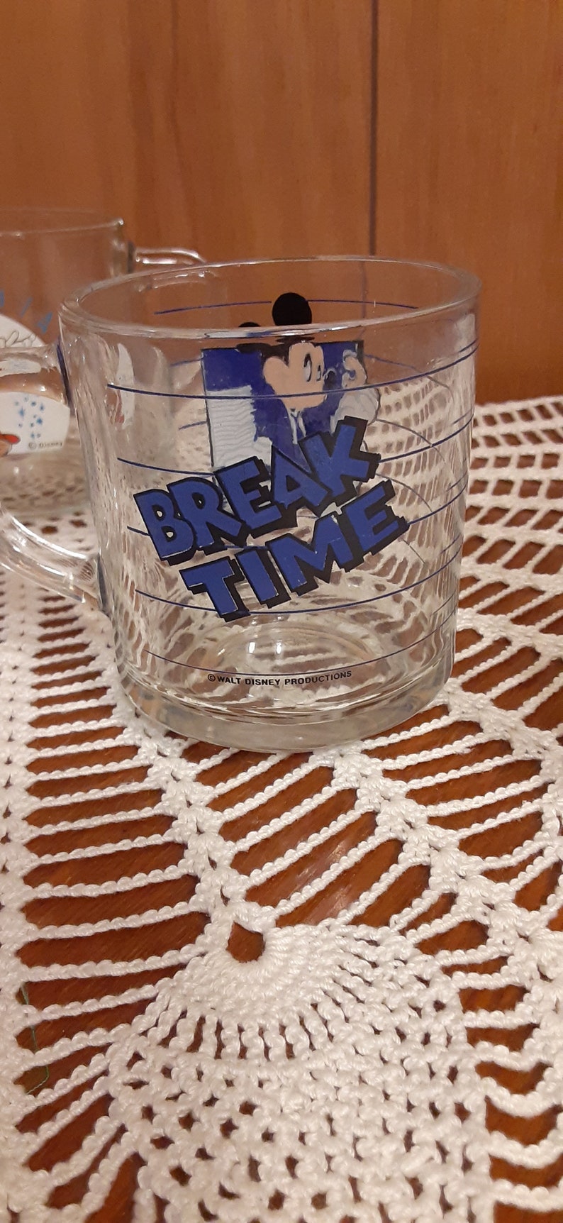 Puede incluir: Una taza de vidrio transparente con un dise&ntilde;o azul y blanco con Mickey Mouse y el texto "Break Time". La taza tiene un asa y est&aacute; decorada con l&iacute;neas azules.