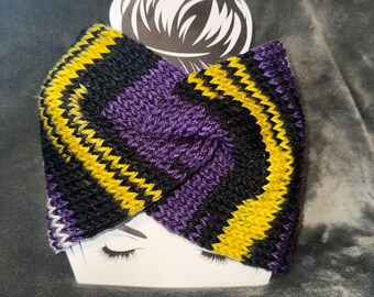 May include: A knitted headband in black, purple, and yellow zig-zag pattern. The headband is displayed on a white card with a graphic of a woman's face and hair. The background is a dark gray, textured fabric.