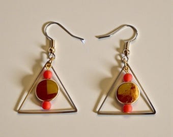 Könnte beinhalten: Ein Paar Ohrringe mit geometrischem Design. Jeder Ohrring hat einen silberfarbenen Dreiecksrahmen, einen goldfarbenen kreisförmigen Anhänger und zwei kleine rote Perlen. Die Ohrringe haben einen Hakenverschluss.