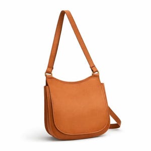 Könnte beinhalten: Eine hellbraune Umhängetasche mit geschwungenem Überschlag und verstellbarem Riemen. Die Tasche hat ein schlichtes, minimalistisches Design mit einem einzigen Hauptfach und einem langen Riemen zum Über-der-Schulter- oder Crossbody-Tragen. Die Tasche ist aus glattem, lederähnlichem Material.