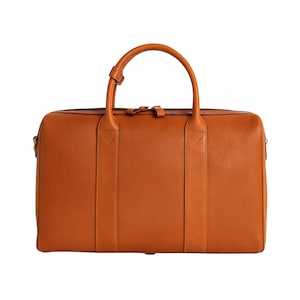 May include: A rectangular, tan leather duffel bag with a top handle and a zipper closure. The bag has a structured design with vertical leather strips on the front and back. The handle is secured with a buckle.