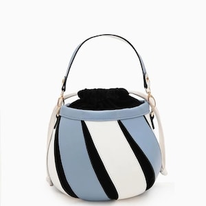Puede incluir: Un elegante bolso tipo cubo con un diseño único. El bolso presenta un patrón de bloques de color con secciones en azul claro, blanco y negro. Tiene un asa superior y un cierre de cordón. El interior del bolso es negro.