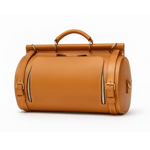 May include: A tan leather duffel bag with a top handle and a cylindrical design. The bag features a front pocket with a zipper, side straps, and gold-colored hardware. The bag is designed for travel.