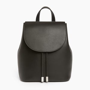 May include: A black backpack with a curved flap and a top handle. The bag features a drawstring closure with silver metal details. The backpack is made of a smooth, solid material.