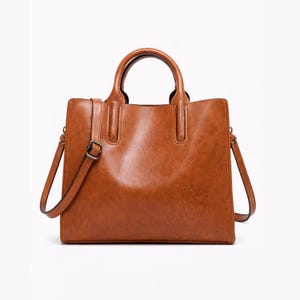 May include: A brown leather tote bag with a top handle and a detachable shoulder strap. The bag has a rectangular shape with a structured design and a silver-colored buckle on the strap. The bag is made of a smooth, shiny material.
