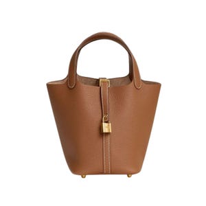 Könnte beinhalten: Eine braune Lederhandtasche mit einem oberen Griff und einem goldfarbenen Schlossverschluss. Die Tasche hat eine strukturierte Eimerform mit flachem Boden und kleinen goldenen Füßen. Weiße Nähte akzentuieren die Nähte.