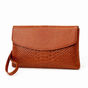 May include: A brown leather clutch with a textured, reptile-like pattern. The clutch has a flap closure and a wrist strap. The color is a warm, medium brown. The overall design is simple and elegant.
