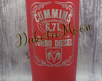 Op de afbeelding: Een rode roestvrijstalen beker met een zilveren gegraveerd ontwerp met de tekst "Cummins 6.7L Turbo Diesel" met een ramlogo.