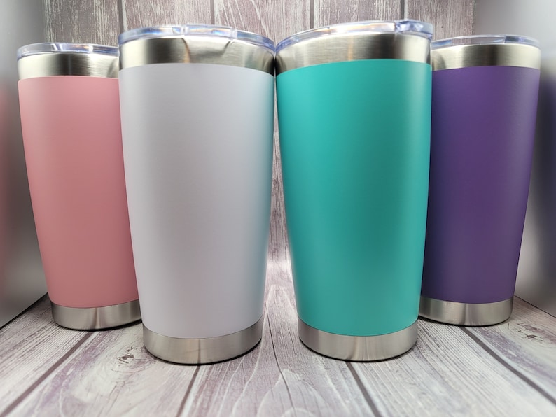 Op de afbeelding: Vier roestvrijstalen bekers met deksels. De bekers zijn in verschillende kleuren: roze, wit, turquoise en paars.