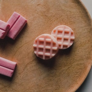 Peut inclure: Des bonbons en forme de gaufre roses et blancs sur une surface en bois.