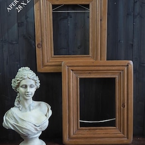 Puede incluir: Dos marcos de fotos rectangulares de madera con acabado marrón medio y moldura escalonada, con un alambre blanco para colgar en la parte posterior. El texto en la parte superior izquierda dice APERTURE 28 X 21. Un busto blanco de color piedra.