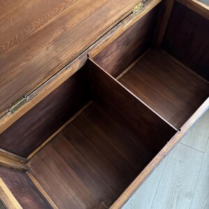 May include: A rectangular wooden storage chest with an open hinged lid, featuring a natural brown wood grain finish and a central vertical divider that separates the interior into two distinct storage compartments with visible metal hinges.