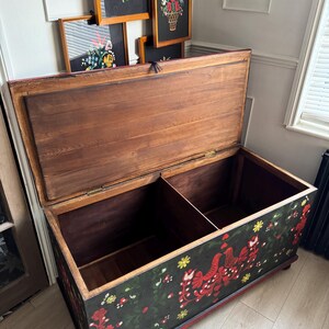 May include: A rectangular wooden storage chest with an open lid, featuring a black exterior painted with red birds, green vines, and yellow flowers. The interior is divided into two sections with natural wood grain panels and metal hinges.