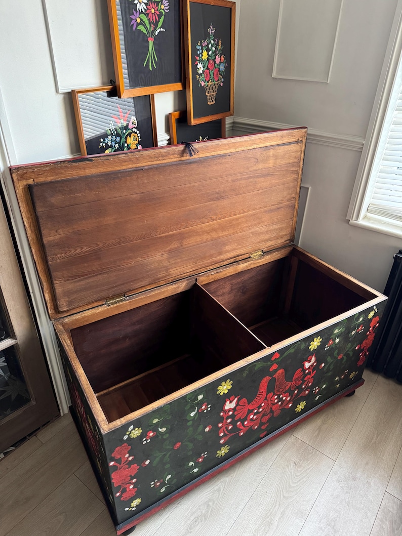 May include: A rectangular wooden storage chest with an open lid, featuring a black exterior painted with red birds, green vines, and yellow flowers. The interior is divided into two sections with natural wood grain panels and metal hinges.