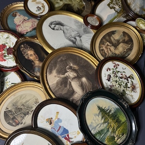 Puede incluir: Una colección de obras de arte antiguas enmarcadas, que incluyen marcos ovalados y redondos. Las obras de arte presentan retratos, paisajes y bordados florales. Los marcos varían en color, incluyendo dorado, marrón y negro, con detalles ornamentados.