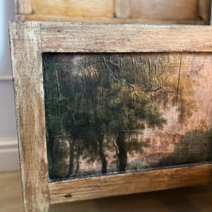 Peut inclure: Banc en bois avec une peinture de paysage sur le panneau avant. La peinture repr&eacute;sente des arbres dans une for&ecirc;t avec une palette de couleurs sourdes de verts, de bruns et de touches de rose. Le banc a un cadre en bois brun clair vieilli.