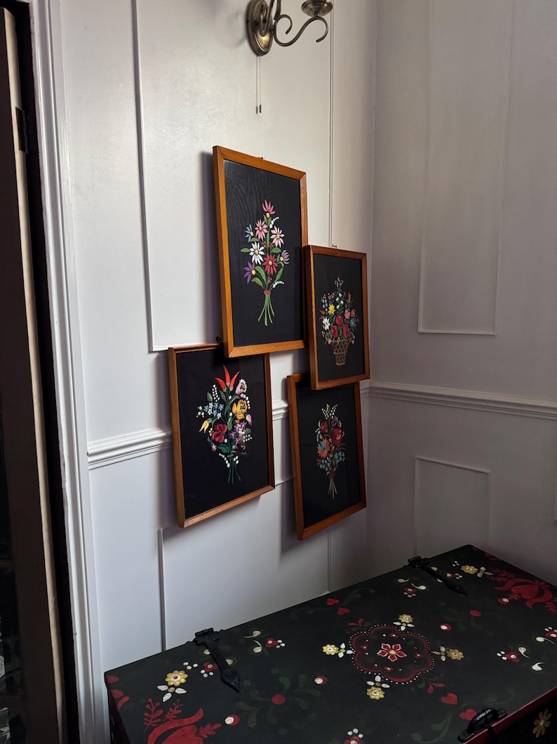 May include: Four rectangular wall art pieces in light wood frames, each featuring a black background with a colorful floral bouquet illustration. The flowers are depicted in shades of red, white, yellow, blue, and pink with green stems and leaves.