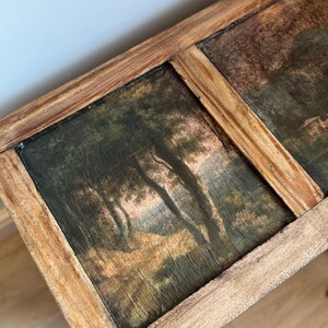 Peut inclure: Une &oelig;uvre d'art rectangulaire encadr&eacute;e de bois, pr&eacute;sentant deux peintures de paysages. Les peintures repr&eacute;sentent des arbres et du feuillage dans des tons verts, bruns et dor&eacute;s. Le cadre en bois a une finition naturelle.