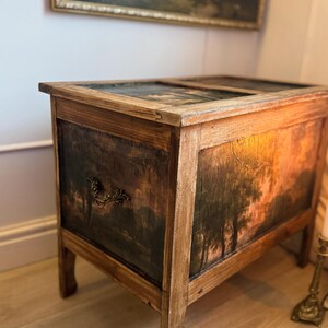 Peut inclure: Un coffre ancien en bois avec une peinture de paysage sur le devant et les c&ocirc;t&eacute;s. Le coffre a une finition marron fonc&eacute; avec une poign&eacute;e d&eacute;corative et repose sur quatre pieds. Le dessus du coffre est &eacute;galement peint avec une sc&egrave;ne de paysage.
