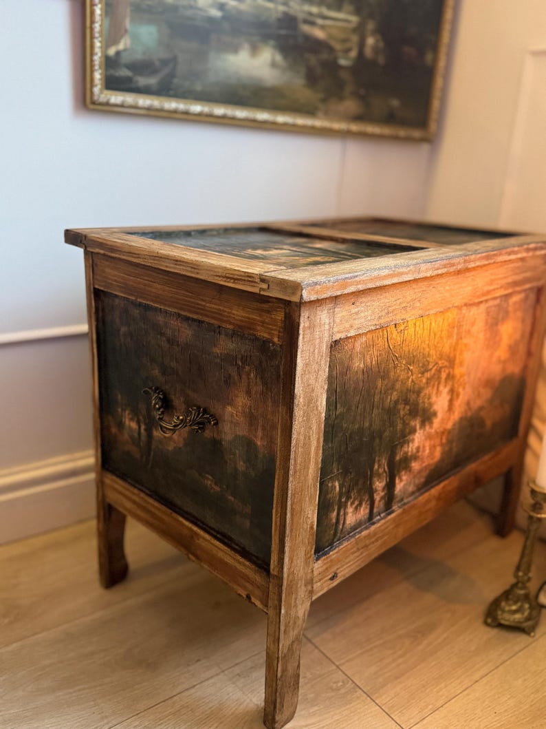 Peut inclure: Un coffre ancien en bois avec une peinture de paysage sur le devant et les c&ocirc;t&eacute;s. Le coffre a une finition marron fonc&eacute; avec une poign&eacute;e d&eacute;corative et repose sur quatre pieds. Le dessus du coffre est &eacute;galement peint avec une sc&egrave;ne de paysage.