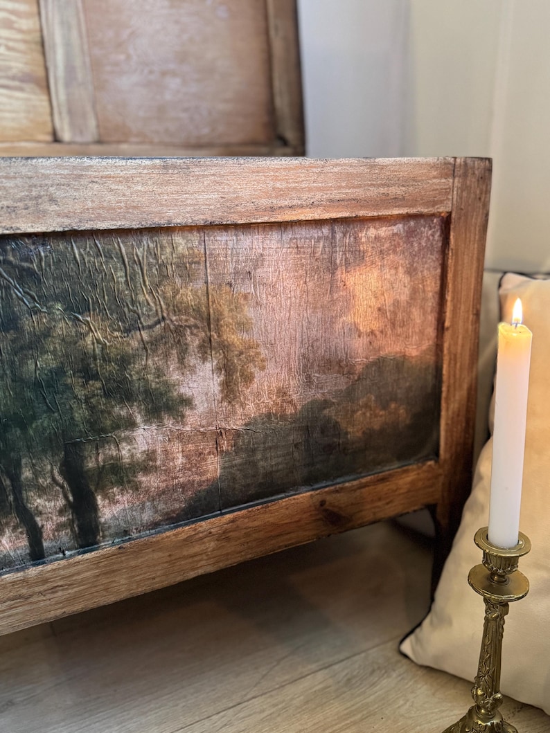 Peut inclure: Gros plan sur un banc ancien en bois avec une peinture de paysage sur le panneau avant. La peinture repr&eacute;sente des arbres et un coucher de soleil. Une bougie allum&eacute;e dans un bougeoir dor&eacute; est au premier plan.