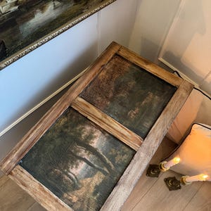 Peut inclure: Table basse rectangulaire en bois avec deux peintures de paysage encadr&eacute;es. Les peintures pr&eacute;sentent une sc&egrave;ne de for&ecirc;t aux tons verts et bruns. La table a une finition marron clair vieillie et repose sur un sol en bois clair.