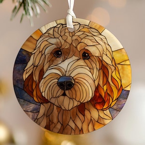 Könnte beinhalten: Runder Weihnachtsschmuck mit einer Buntglas-Illustration eines Hundegesichts. Der Schmuck hat ein weißes Band zum Aufhängen. Der Hund hat braunes Fell, eine blaue Nase und einen gelb, orange und blauen Hintergrund.
